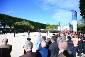 Pompiers en uniforme alignés sur une place publique devant une foule lors d'une cérémonie officielle.