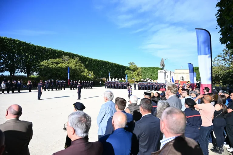Pompiers en uniforme alignés sur une place publique devant une foule lors d'une cérémonie officielle.