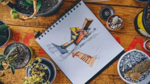 Carnet à croquis ouvert sur une table en bois montrant un dessin d'architecture coloré entouré de plantes.