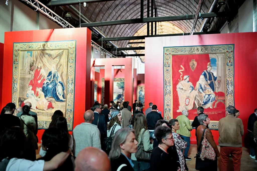 Foule de visiteurs admirant des tapisseries médiévales monumentales sur des parois d'exposition rouges.