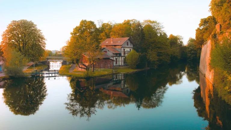 Une maison traditionnelle au bord de l'eau à Metz lors d'un coucher de soleil doré.