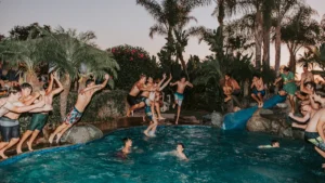 Un groupe de jeunes sautant avec enthousiasme dans une piscine au crépuscule.