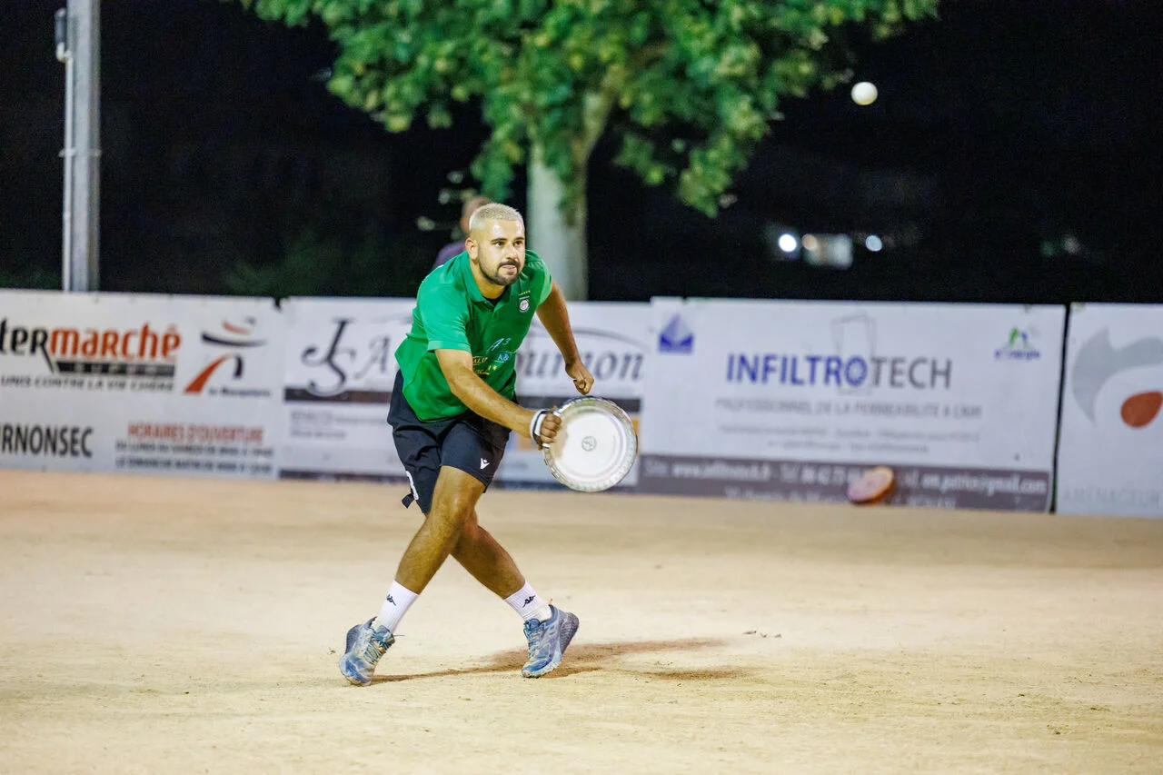 Un homme en maillot vert tenant un tambourin sur un terrain de sport sablonneux.
