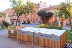 Bacs de compostage collectif en bois et métal sur une place arborée à Toulouse.