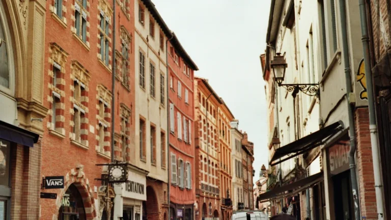 Une rue animée de Toulouse avec ses façades emblématiques en briques rouges sous un ciel clair.