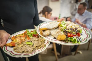Une personne tient deux grandes assiettes garnies de pâtes crémeuses, viande panée et salade fraîche.