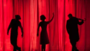 Trois silhouettes mystérieuses se découpent derrière un rideau de théâtre rouge intense, évoquant une atmosphère de thriller.