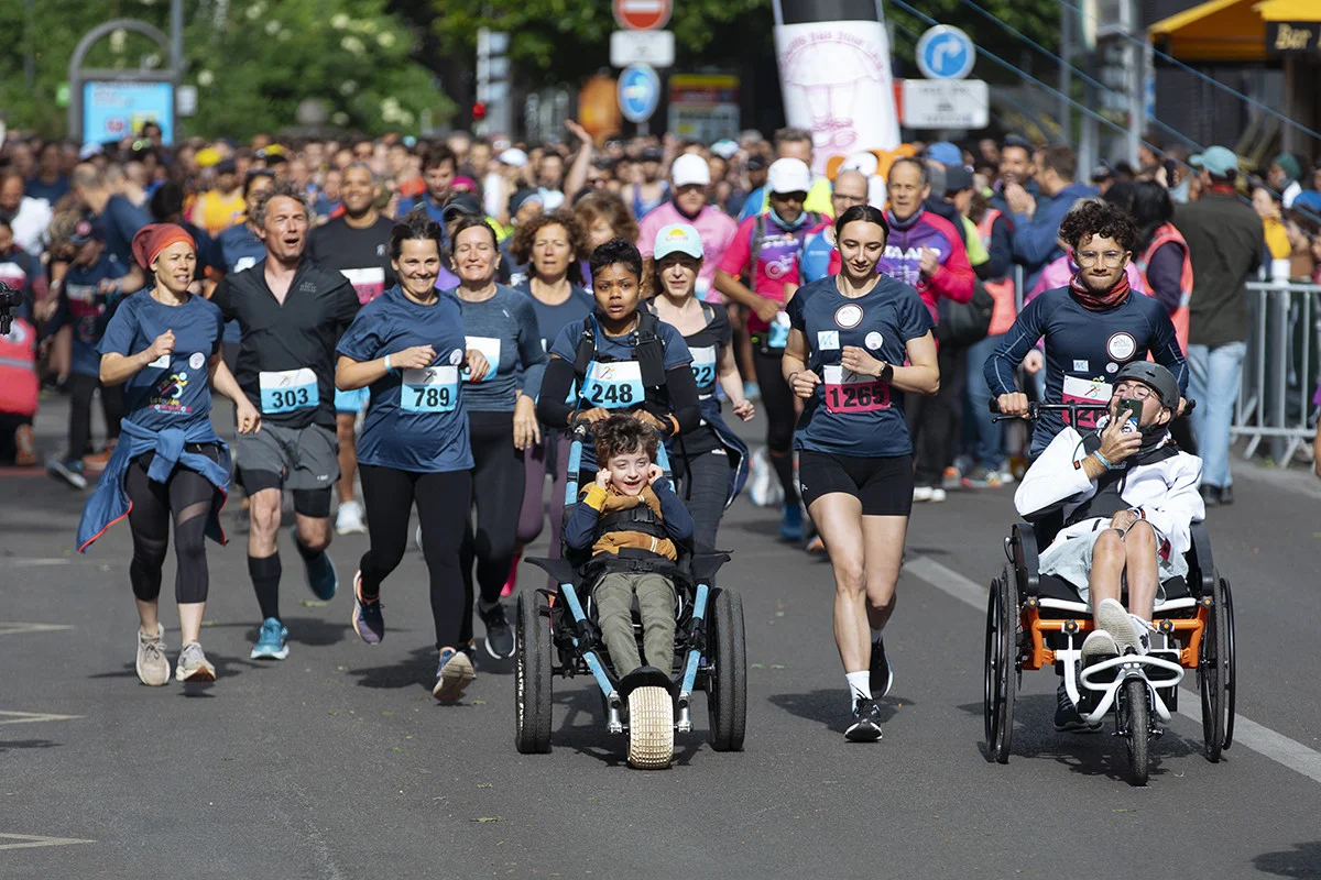 Une foule de coureurs participe à un marathon urbain avec des personnes en fauteuil roulant.