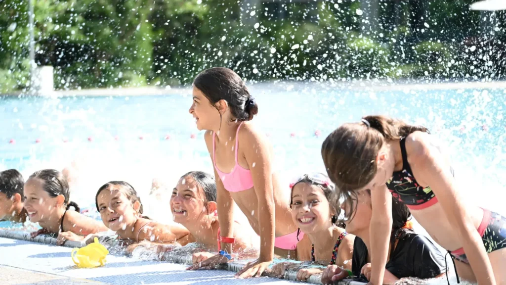 Groupe d'enfants souriants s'amusant au bord d'une piscine sous des éclaboussures d'eau cristalline.