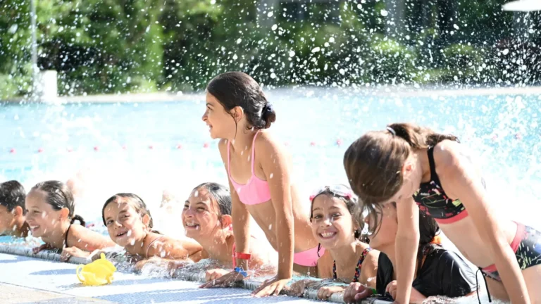 Groupe d'enfants souriants s'amusant au bord d'une piscine sous des éclaboussures d'eau cristalline.