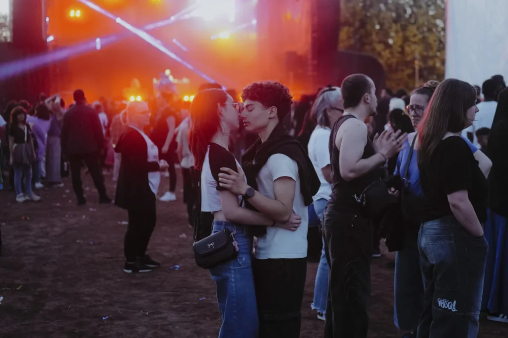 Un jeune couple s'embrasse tendrement au milieu d'une foule lors d'un festival de musique nocturne.