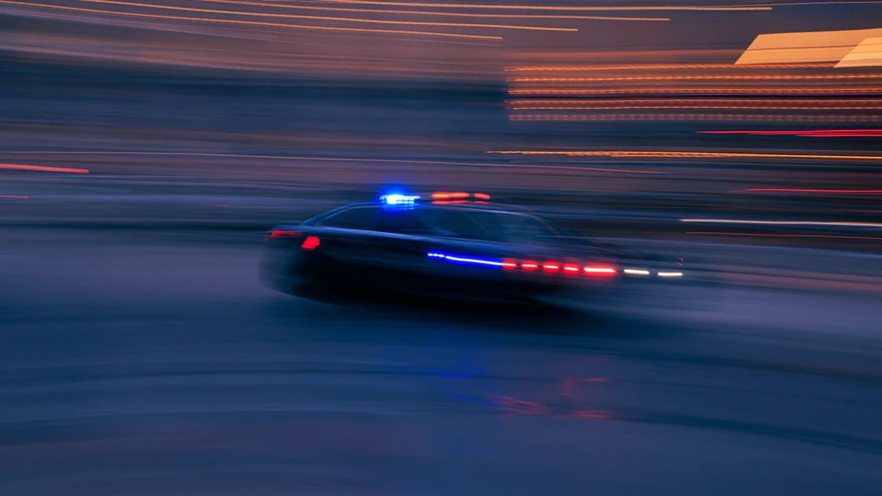 Une voiture de police patrouillant rapidement dans une rue sombre en ville.