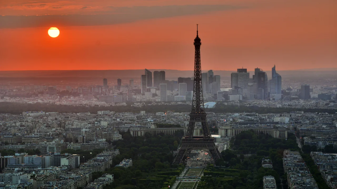 Vue aérienne de la Tour Eiffel sous un soleil couchant intensément orange et chaud.