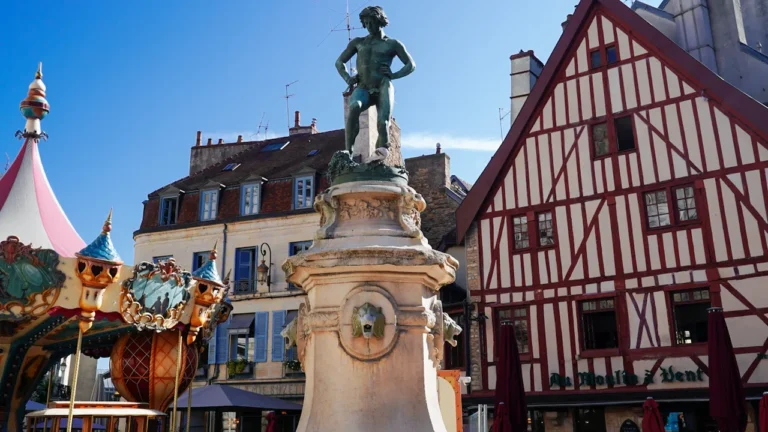 Statue en bronze sur une place historique de Dijon avec maisons à colombages.