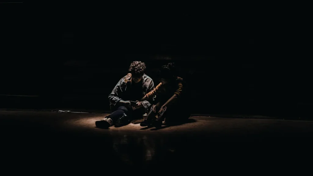 Deux musiciens assis sur une scène sombre, éclairés par un projecteur ponctuel.