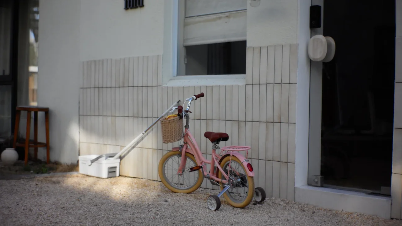 Un vélo rose pour enfant garé devant un bâtiment moderne à l'architecture claire.