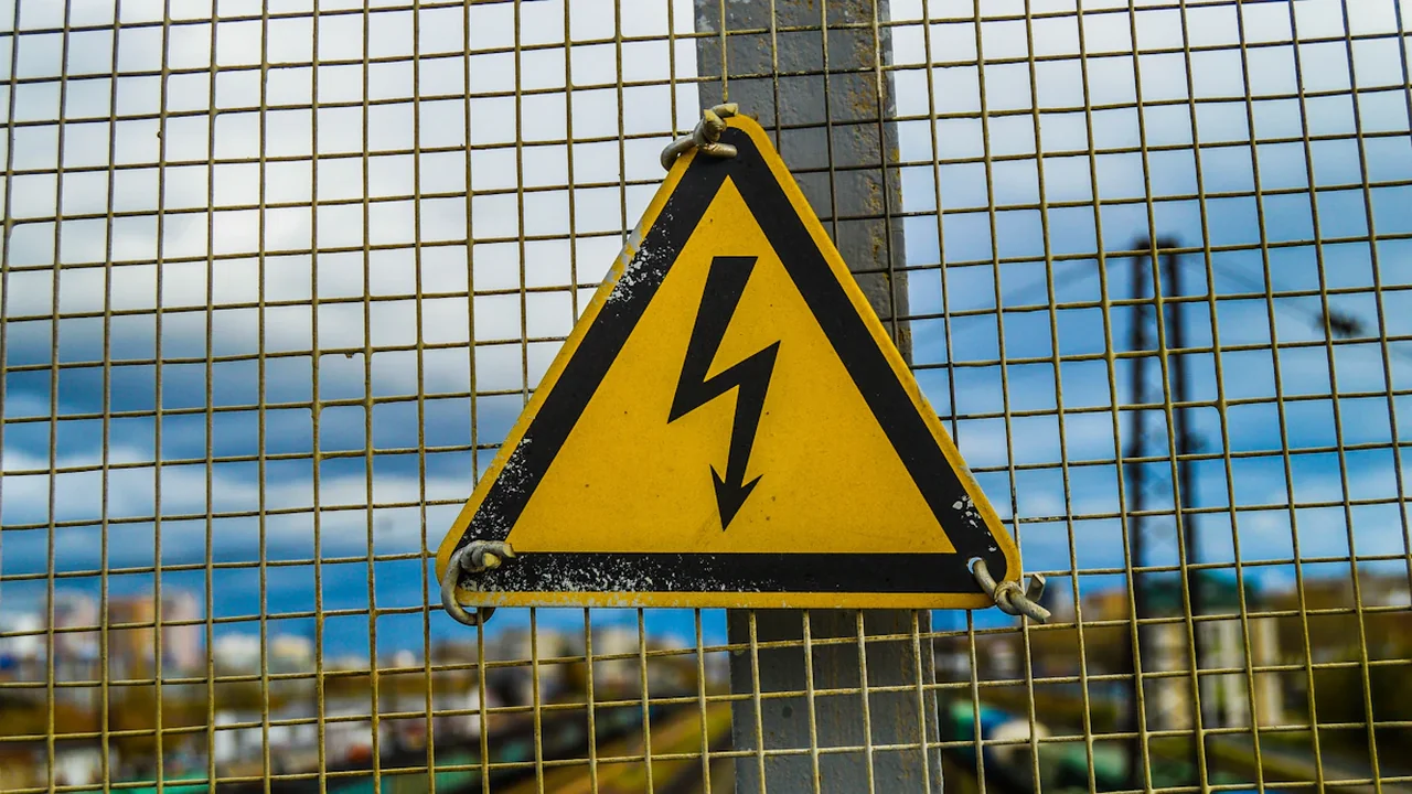 Panneau de danger électrique jaune sur une clôture métallique grillagée en ville.