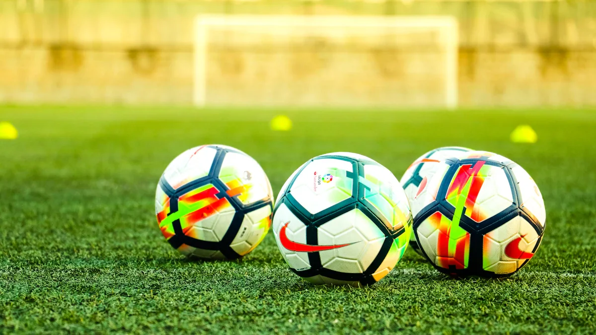 Trois ballons de football posés sur une pelouse verte avant une rencontre sportive importante.