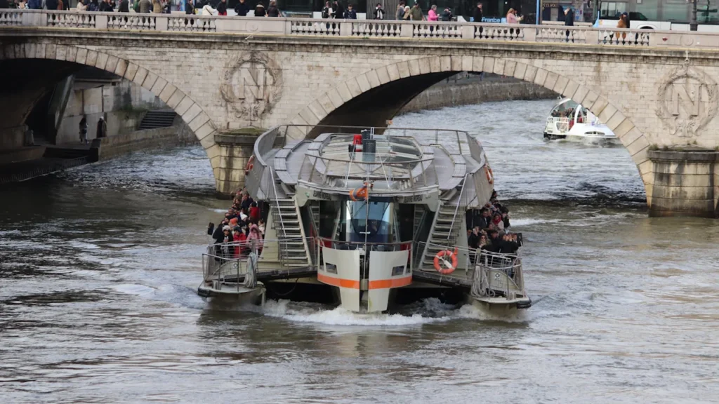 Un bateau de tourisme circule sous un pont en pierre sur la Seine à Paris.