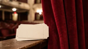 Deux tickets vierges posés sur un rebord en bois devant un rideau rouge.