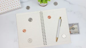 Cahier ouvert avec pièces de monnaie, stylo et billets pour la gestion financière personnelle.