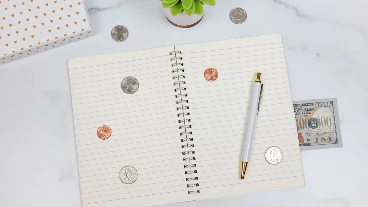 Cahier ouvert avec pièces de monnaie, stylo et billets pour la gestion financière personnelle.