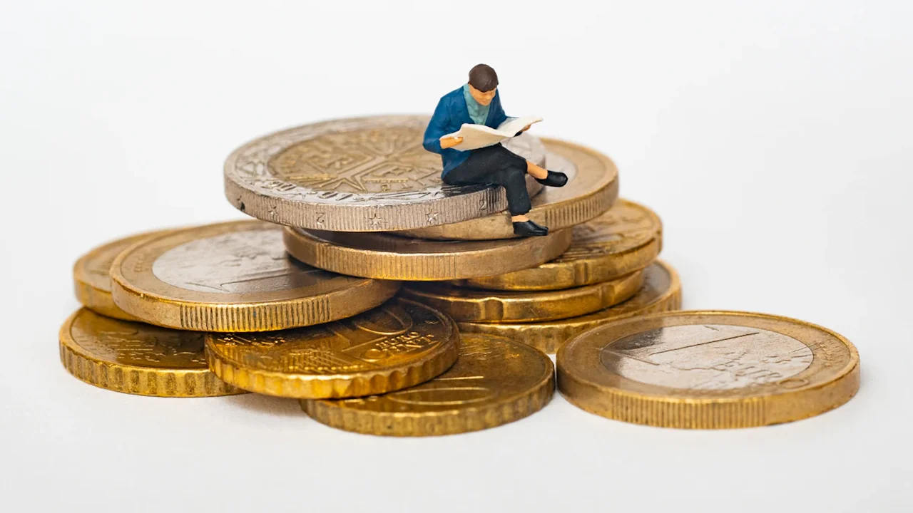 Une figurine miniature assise sur une pile de pièces d'euro lisant un journal.
