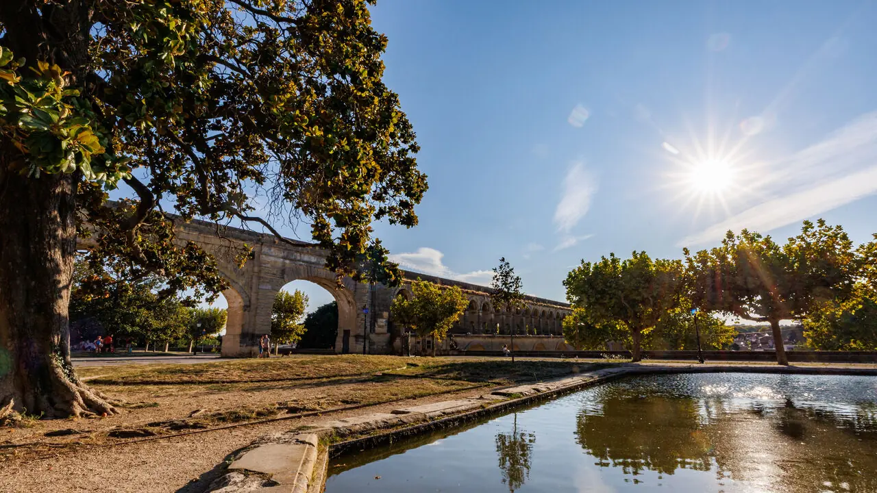 Ancien aqueduc romain en pierre près d'un bassin d'eau sous un soleil éclatant.