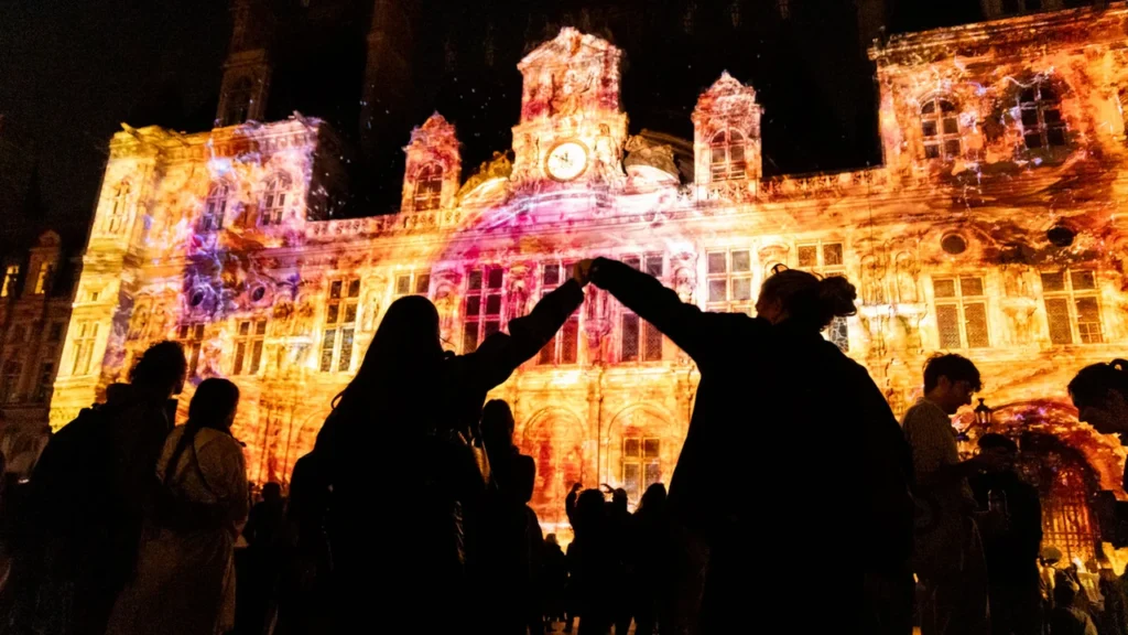 Silhouette de personnes face à un bâtiment illuminé par des projections artistiques nocturnes.