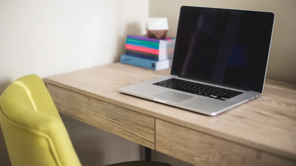 Un ordinateur portable posé sur un bureau en bois avec des livres colorés.