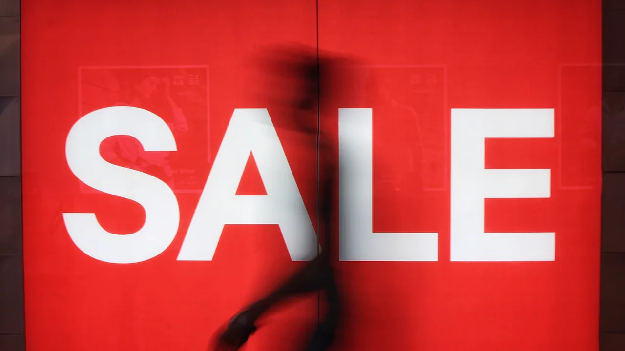 Une enseigne rouge lumineuse affichant le mot SALE avec une silhouette humaine floue.