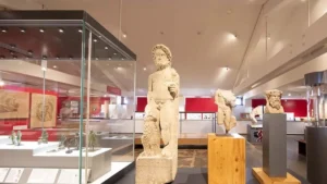 Statue en pierre de style antique exposée dans une salle de musée moderne éclairée.