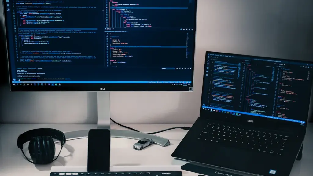 Bureau de travail moderne avec ordinateur portable et écran affichant du code informatique.