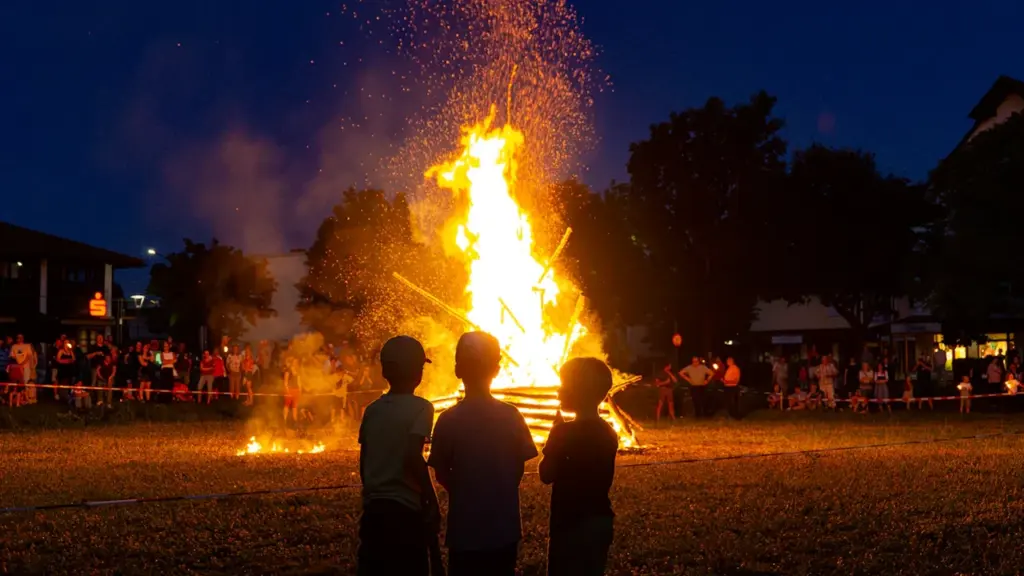 Trois enfants regardent un grand feu de joie festif en soirée à Caen.