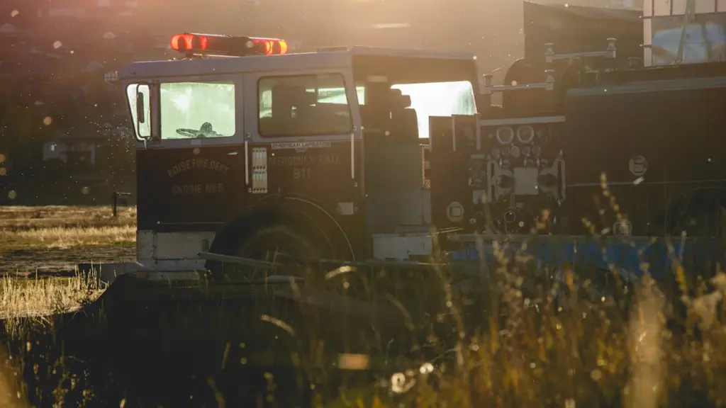 Un camion de pompiers avec gyrophares allumés lors d'un coucher de soleil estival.