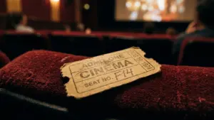 Un vieux ticket de cinéma posé sur un siège rouge devant une salle sombre.