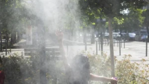 Une personne vue de dos lève la main dans un nuage de brume rafraîchissante.