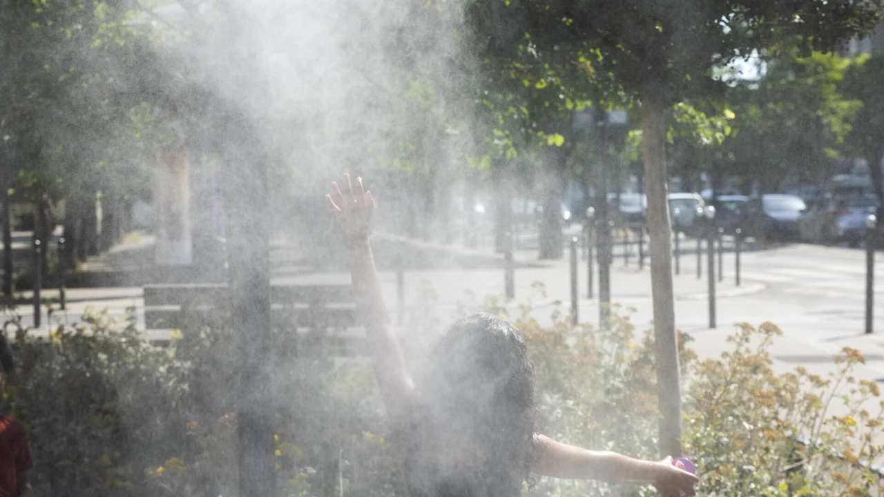 Une personne vue de dos lève la main dans un nuage de brume rafraîchissante.