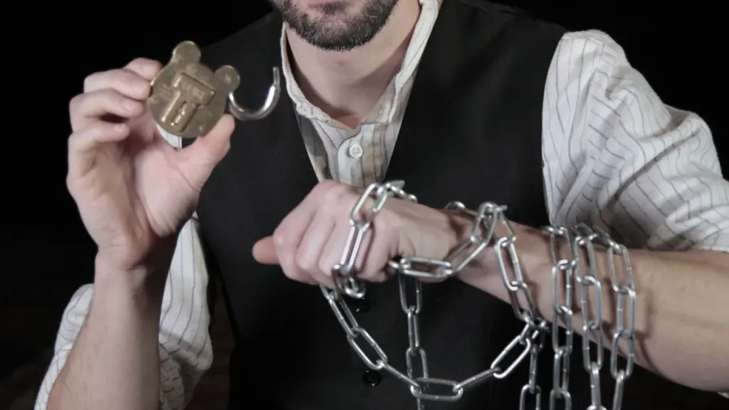 Un homme barbu tient un cadenas ouvert et montre ses poignets entravés par des chaînes.