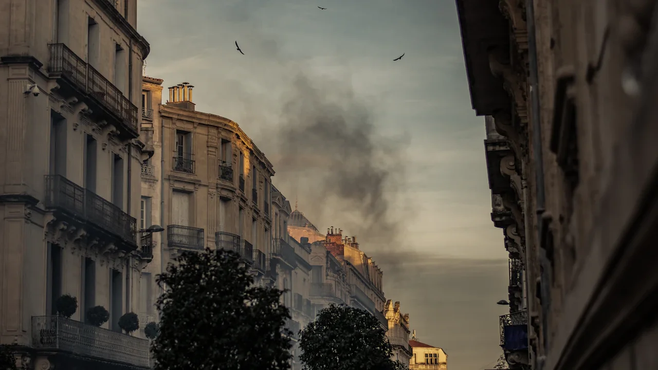 Panache de fumée noire s'élevant au-dessus d'immeubles résidentiels en zone urbaine dense.
