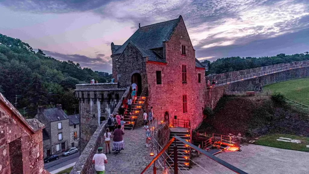 Vue plongeante sur un château médiéval en pierre illuminé par des lanternes au crépuscule.