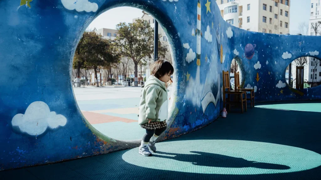 Une enfant traverse un tunnel coloré dans une aire de jeux urbaine.