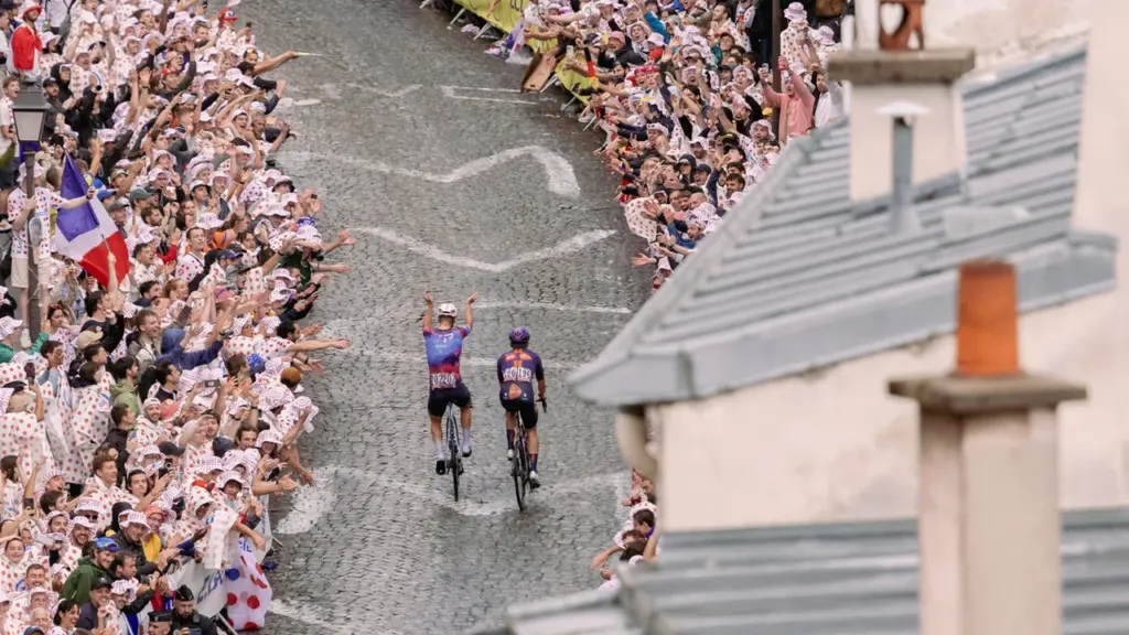 Deux cyclistes montent une rue pavée entourée d'une foule enthousiaste agitant des drapeaux français.