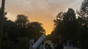 Un groupe de personnes observe le ciel avec des télescopes durant un coucher soleil.