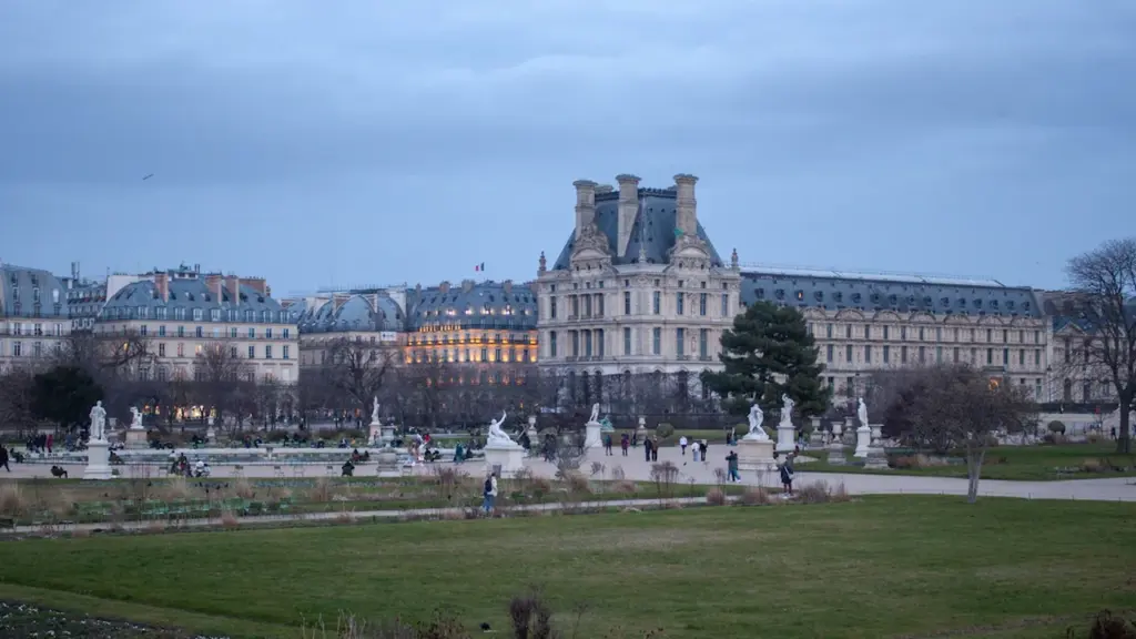 Grand bâtiment historique français entouré de jardins bien entretenus par une journée grise.