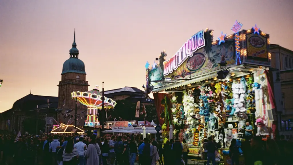 Ambiance festive avec manèges et stands de jeux devant une église au crépuscule.