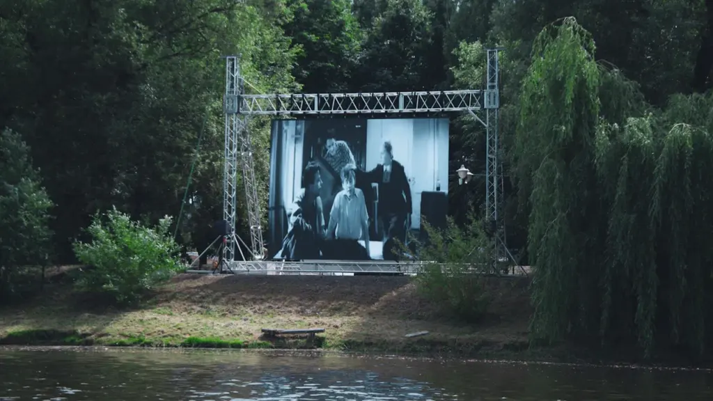 Grand écran de cinéma en plein air installé au bord d'un parc verdoyant.