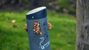 Un cendrier public rempli de mégots de cigarettes sur un trottoir urbain.