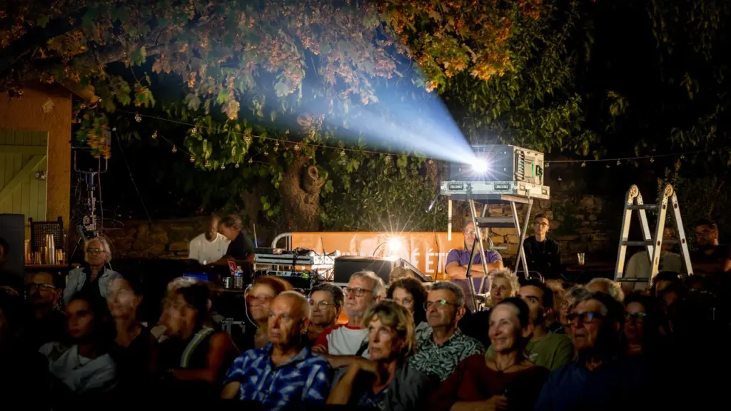 Un projecteur de cinéma projette un faisceau lumineux au-dessus d'un public attentif en extérieur.