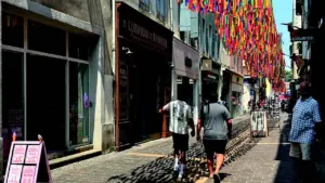 Une rue piétonne pavée décorée de nombreux rubans colorés suspendus au-dessus des passants.